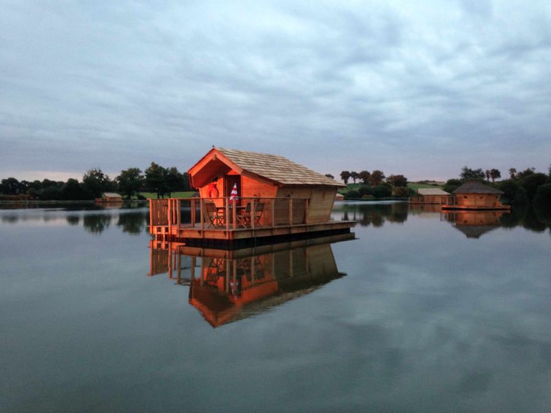 Cabane flottante au bord dun lac, illuminée par un doux coucher de soleil.