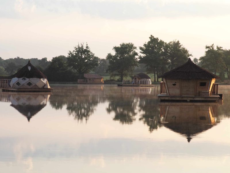 Hébergements insolites sur leau, avec toits de chaume et reflets dans le lac.