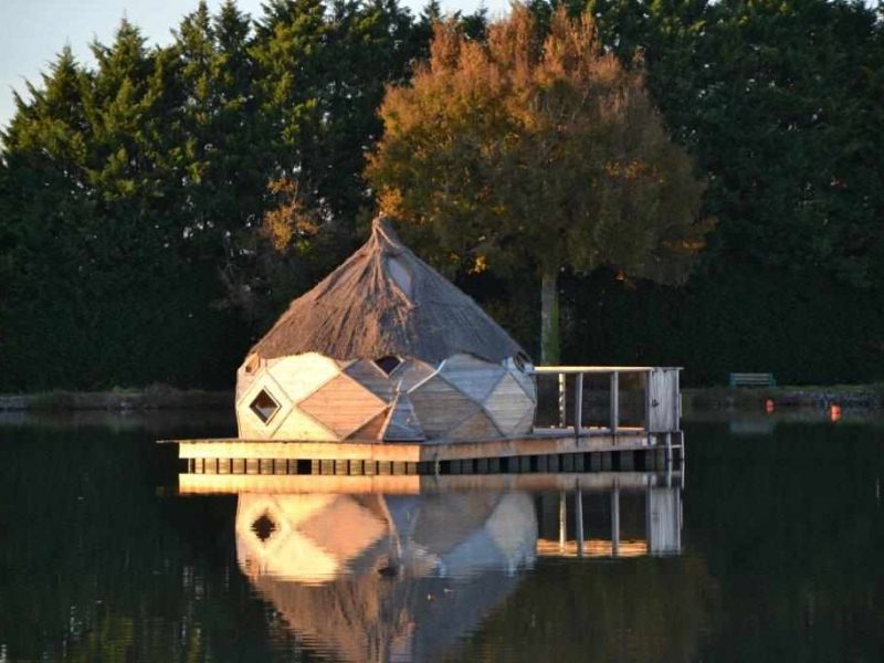 Hébergement insolite en forme de yourte sur un lac, entouré de verdure.
