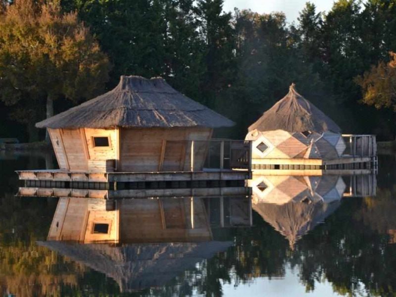 Cabines flottantes en bois avec toits de chaume, reflet sur leau calme.