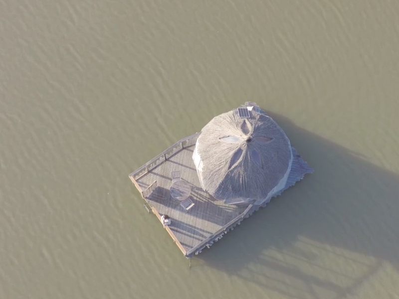 Cabane flottante en bois avec un toit en chaume, entourée deau calme.