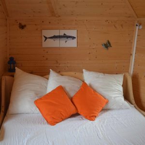 Cabane en bois avec lit douillet et coussins orange, ambiance chaleureuse.