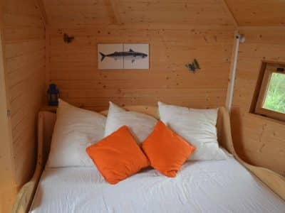 Cabane en bois avec lit douillet et coussins orange, ambiance chaleureuse.