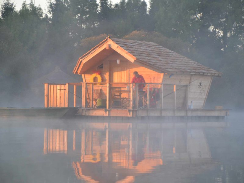 Cabane flottante au bord dun lac, baignée de lumière matinale et entourée de brume.