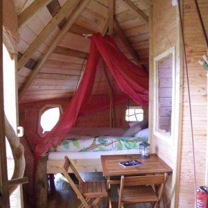 Cabane en bois à Haute-Normandie, avec un lit sous un voile rouge et un coin repas.