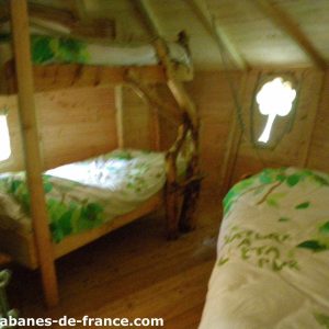 Cabane en bois avec lits superposés et fenêtre en forme de trèfle.