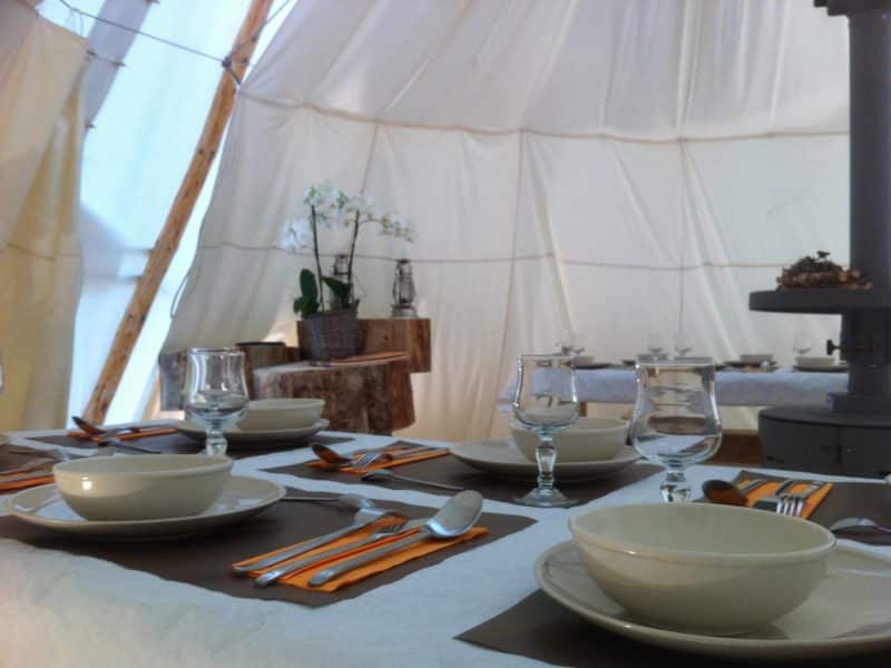 Tente de glamping avec table dressée, vaisselle élégante et ambiance chaleureuse.