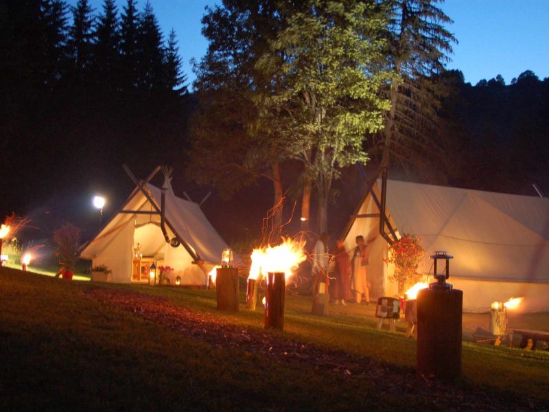 Tentes de glamping illuminées par des lanternes, entourées darbres au crépuscule.