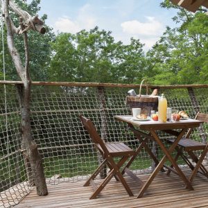 Cabane dans les arbres avec une terrasse en bois et un petit déjeuner en plein air.