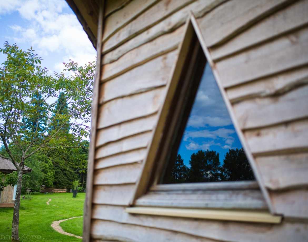 Cabane en bois triangulaire, fenêtre originale reflétant le ciel et la verdure.