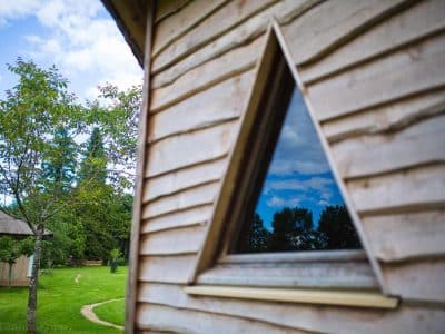 Cabane en bois triangulaire, fenêtre originale reflétant le ciel et la verdure.