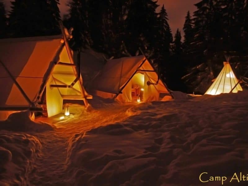 Tentes de glamping illuminées dans un cadre enneigé, offrant une expérience unique.