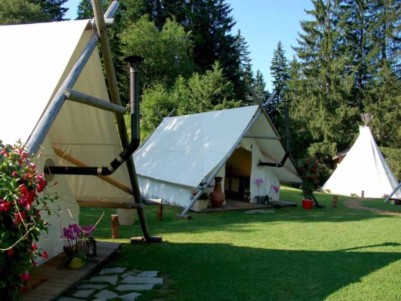 Tentes de glamping entourées de verdure, avec chemin en pierres et fleurs colorées.