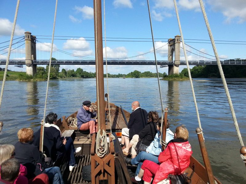 Croisière fluviale sur un bateau traditionnel avec vue sur un pont suspendu.