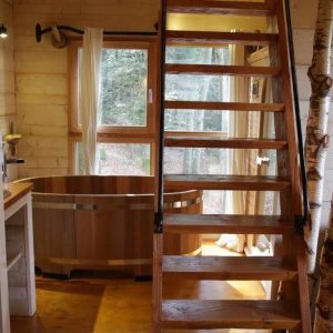 Cabane en bois avec baignoire en bois et escalier en colimaçon, ambiance nature.