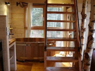 Cabane en bois avec baignoire en bois et escalier en colimaçon, ambiance nature.