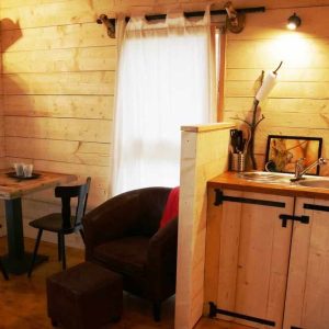 Cabane en bois cosy avec cuisine, table et fauteuil, idéale pour un séjour en Bourgogne.