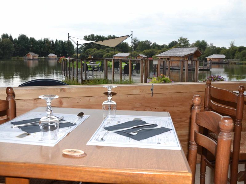 Table en bois avec vue sur des cabanes au bord de leau dans un restaurant.