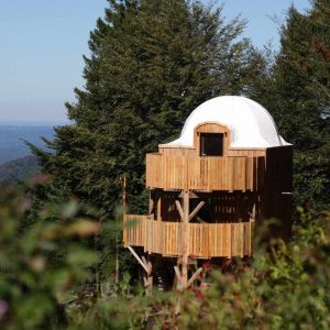 Cabane perchée en bois avec un dôme blanc, entourée de verdure en Bourgogne-Franche-Comté.
