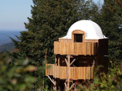 Cabane perchée en bois avec un dôme blanc, entourée de verdure en Bourgogne-Franche-Comté.