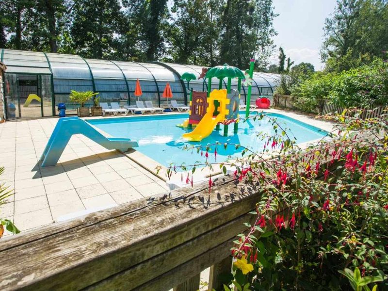 Camping avec piscine extérieure, toboggan coloré et verdure environnante.