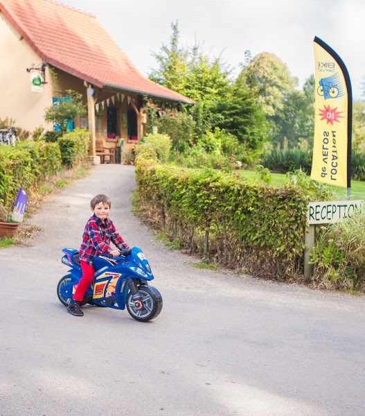 Gîte accueillant avec un enfant sur une moto jouet devant la réception.