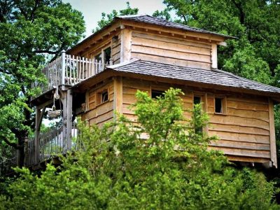 Cabane perchée en bois avec terrasse, entourée darbres verdoyants en Midi-Pyrénées.