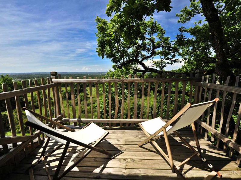 Terrasse en bois dun chalet avec chaises longues et vue sur la nature.