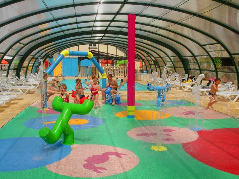 Espace aquatique couvert avec jeux deau colorés pour enfants dans un camping.