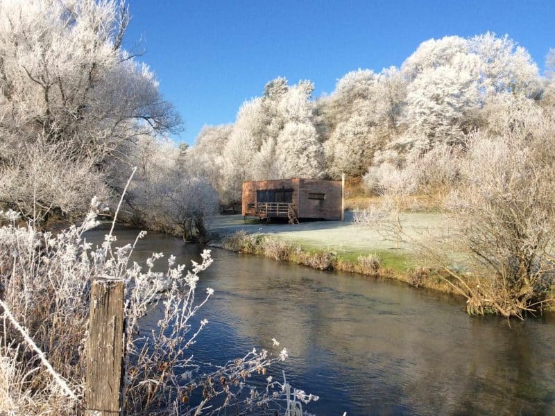 Cabane en bois au bord dune rivière, entourée darbres givrés en Bourgogne.
