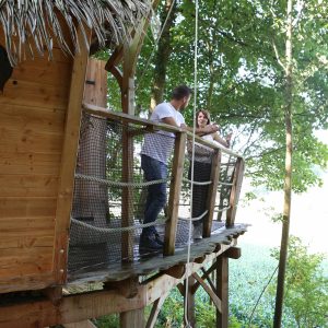 Cabane perchée dans les arbres, avec un balcon en bois et une vue sur la nature.