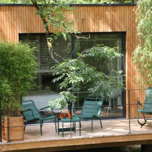 Cabane en bois à Bourgogne avec terrasse et chaises vertes entourée de verdure.