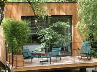 Cabane en bois à Bourgogne avec terrasse et chaises vertes entourée de verdure.