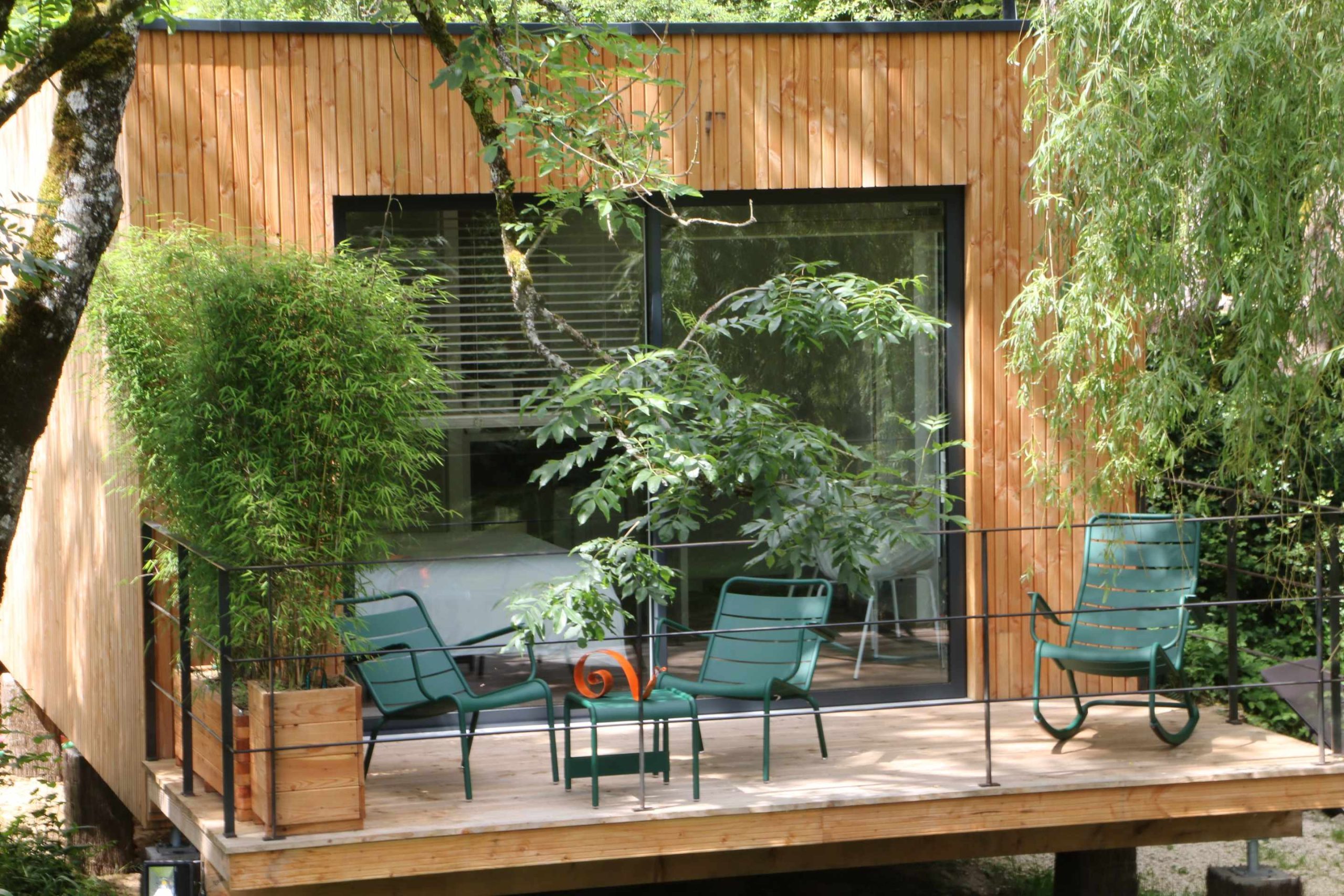 IMG_0977 Cabane en bois à Bourgogne avec terrasse et chaises vertes entourée de verdure.