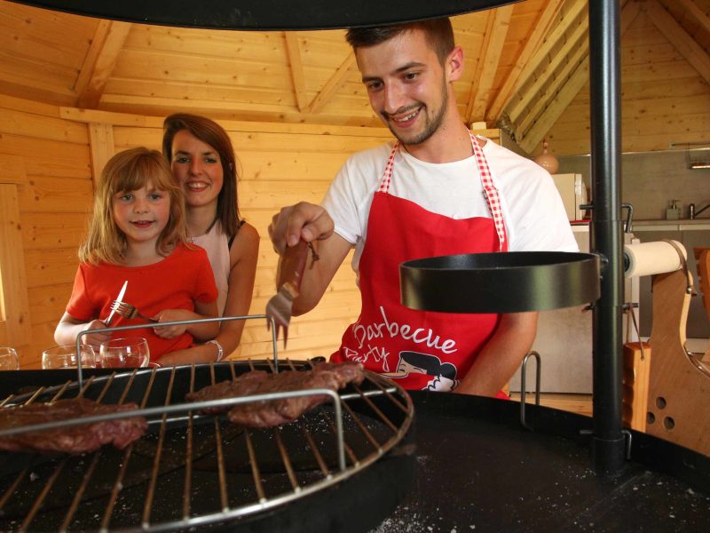 Cabane en bois conviviale avec barbecue, famille en train de cuisiner ensemble.