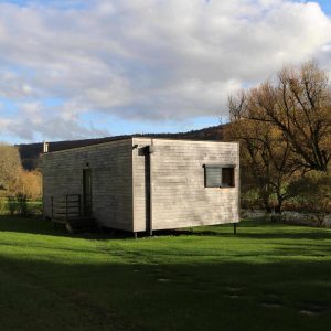 Cabane en bois moderne, entourée de verdure et près dune rivière en Bourgogne.