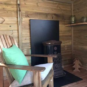 Cabane en bois avec fauteuil confortable et poêle décoratif en métal.
