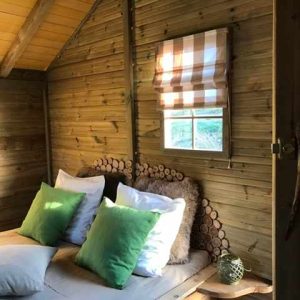 Cabane en bois à Île-de-France, avec un lit douillet et des coussins verts.