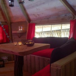 Cabane en bois avec un coin salon cosy, lanternes et rideaux rouges.