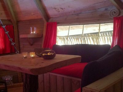 Cabane en bois avec un coin salon cosy, lanternes et rideaux rouges.
