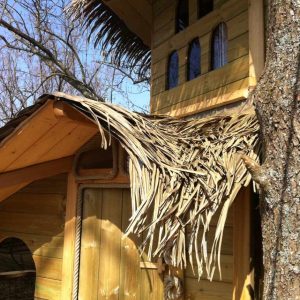 Cabane en bois perchée, toit en feuilles, située en pleine nature en Île-de-France.