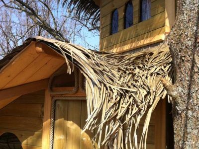 Cabane en bois perchée, toit en feuilles, située en pleine nature en Île-de-France.