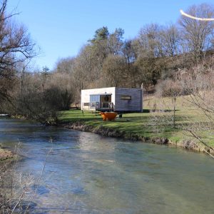 Cabane en bois au bord dune rivière, entourée de verdure en Bourgogne.