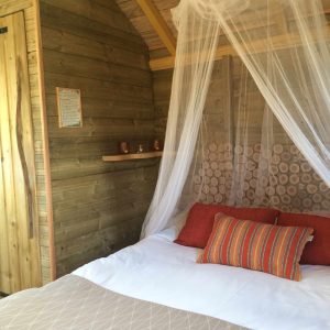 Cabane en bois avec un lit douillet, drapée dun voile léger et décorée de coussins colorés.