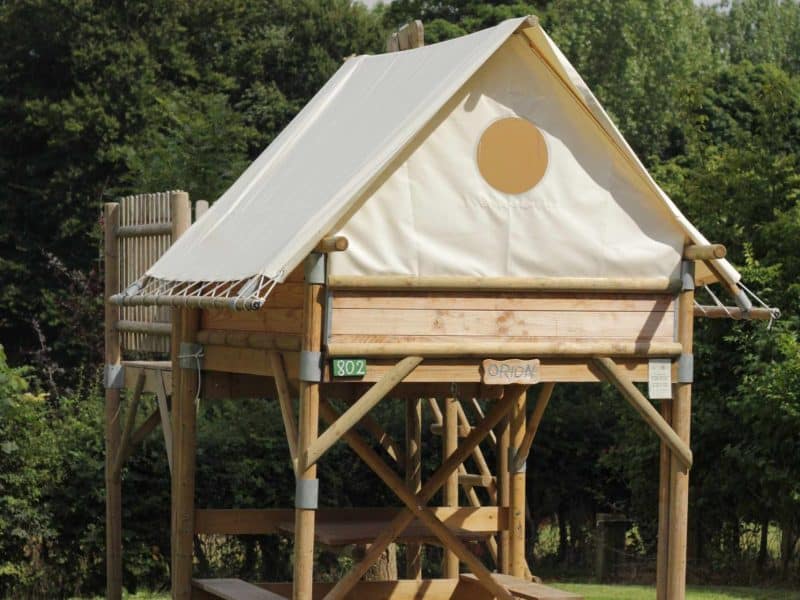 Cabane perchée en bois avec toit en toile, entourée de verdure à Hauts-de-France.