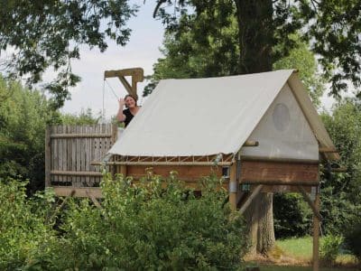 Cabane perchée en bois avec toile, entourée de verdure à Hauts-de-France.