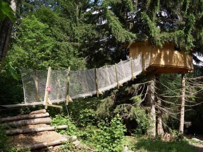 Cabane perchée dans les arbres, accessible par un pont suspendu, au cœur de la nature.