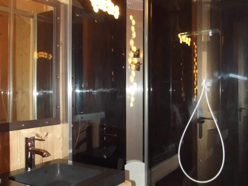 Salle de bain moderne dans un chalet en bois, avec douche vitrée et lavabo en pierre.