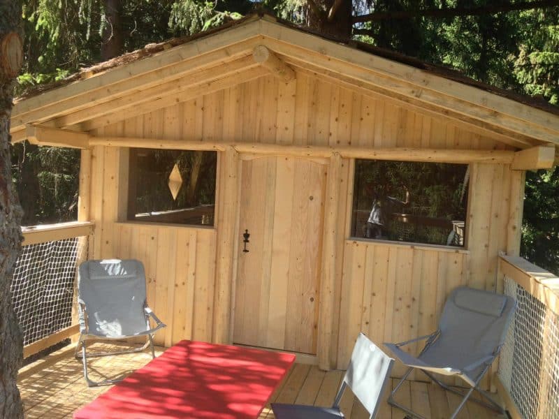 Cabane en bois perchée, avec terrasse en bois et chaises confortables.