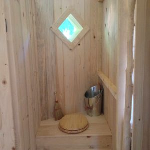 Cabane en bois dans les arbres avec une fenêtre en losange et un coin toilette.